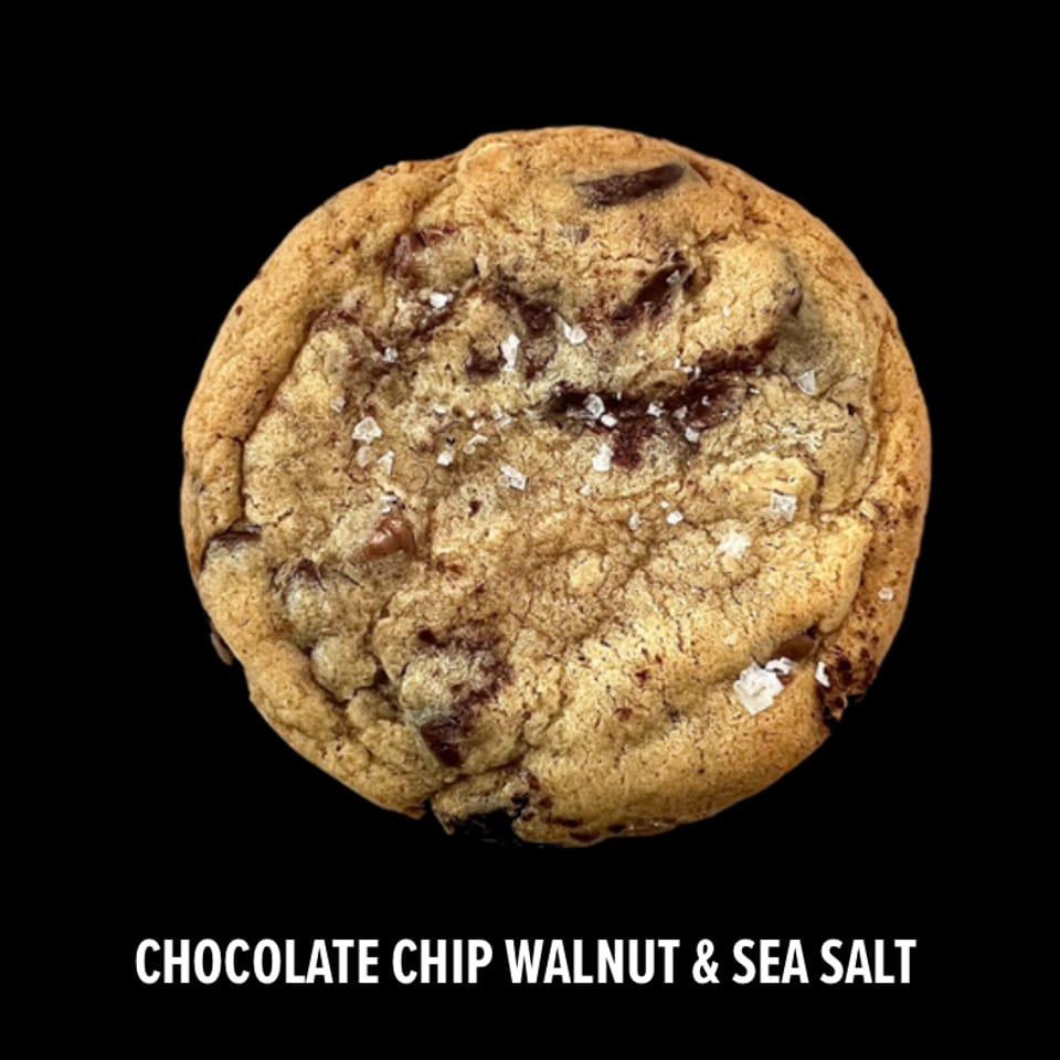 Large chocolate chip walnut cookie sprinkled with sea salt against a black background.