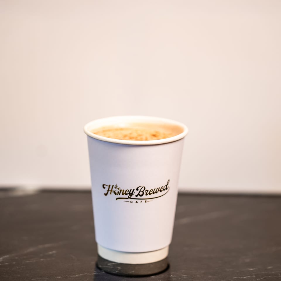 Honey Brew Cafe takeaway cup filled with a frothy coffee drink on a dark reflective table.