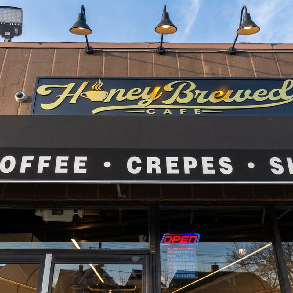 Exterior of HoneyBrewed Cafe featuring signage for coffee, crepes, and sharusts, with an open sign above the entrance.