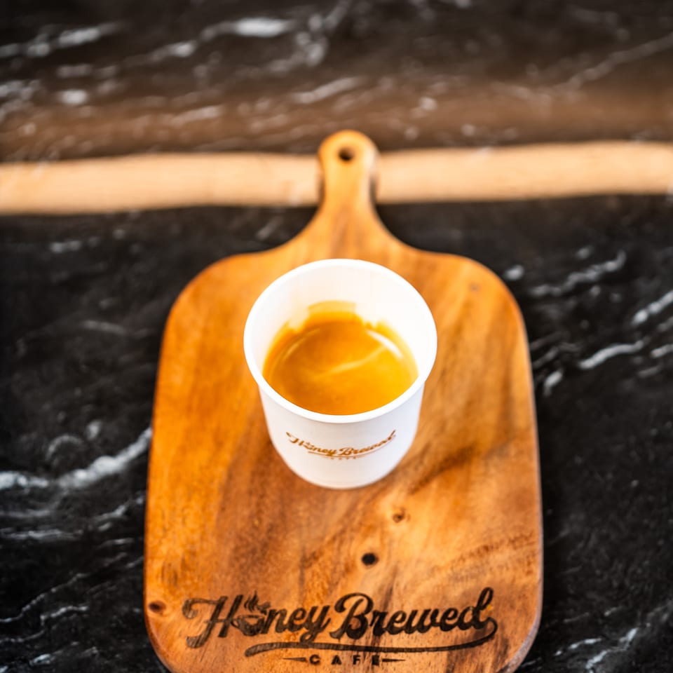 Cup of orange drink on a wooden H Street Brewed Cafe board atop a black marble table.