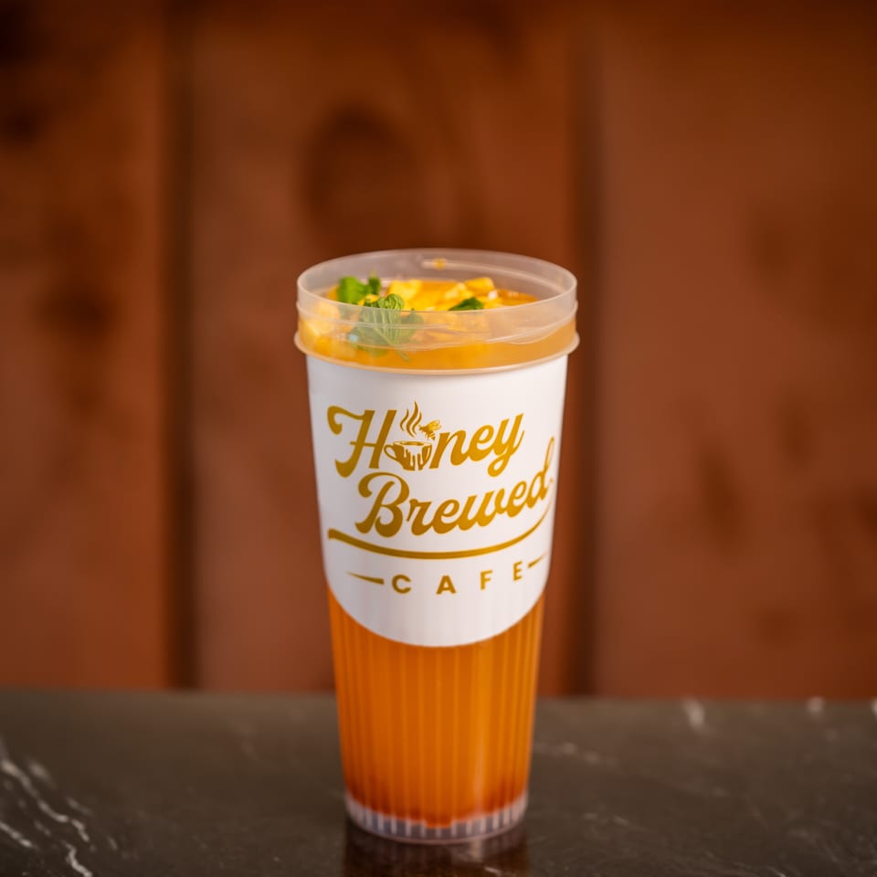 Orange beverage with mint garnish in a Honey Brewed Cafe cup on a dark marble table.