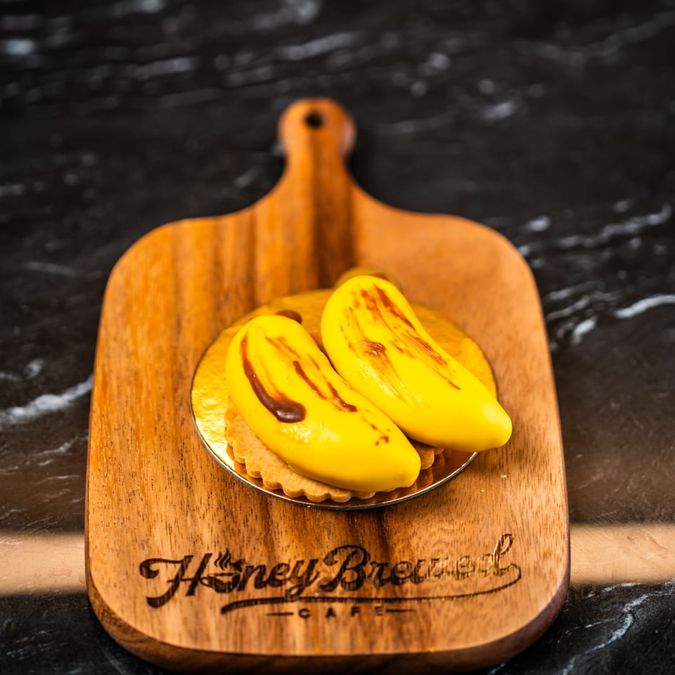 Yellow grilled dessert topped with caramelized fruit sits on a small plate atop a wooden board engraved “Happen Before Cafe.”