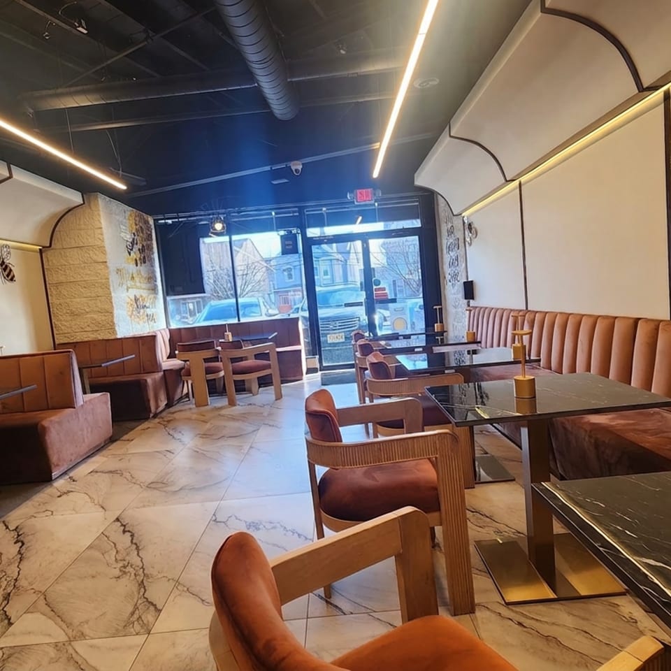 Modern restaurant interior with caramel leather booths, marble tables, wooden chairs, decorative walls, and large street-facing windows.