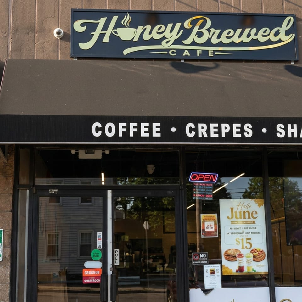 Exterior of HoneyBrewed Cafe with signage for coffee, crepes, shakes, an open sign, and promotional window posters.